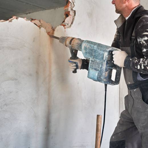 Close up of special powerful hand instrument with percussion mechanism for drilling and breaking walls. Man holding jackhammer and dismantling inner wall in room.